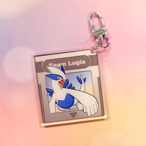 A silver colored game cartridge keychain, retro themed with a character coming out of it
